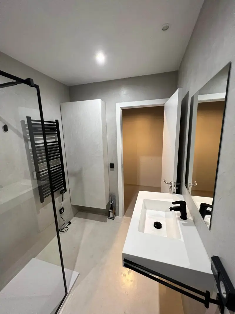 Baño con paredes de microcemento gris, lavabo suspendido y mampara