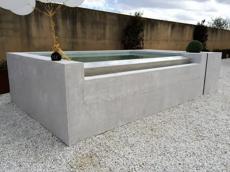 Piscina elevada revestida en microcemento gris sobre un jardín de grava
