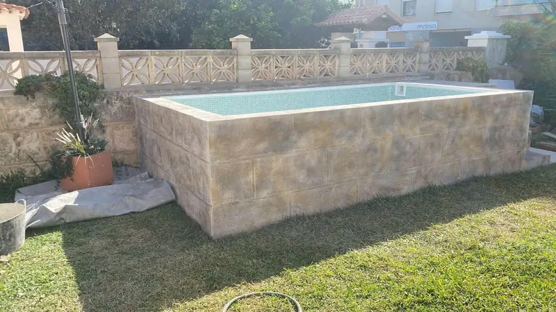 Piscina elevada revestida con acabado de sillería envejecida en un jardín