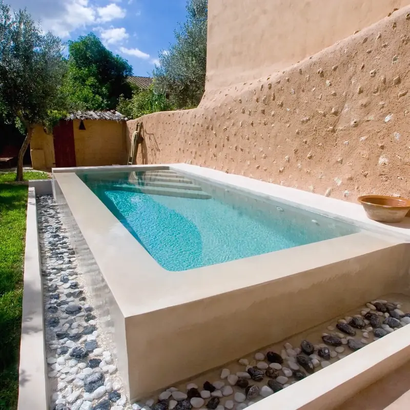 Piscina de microcemento en un patio con muro de acabado tierra y canto rodado