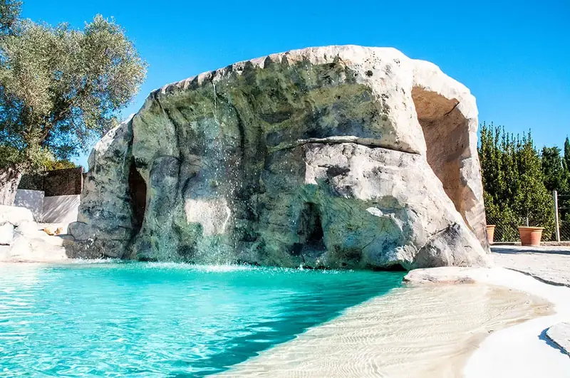 Piscina con entrada tipo playa junto a una gran roca artificial