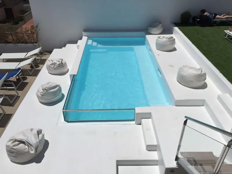 Piscina en una terraza con lateral de cristal y entorno blanco