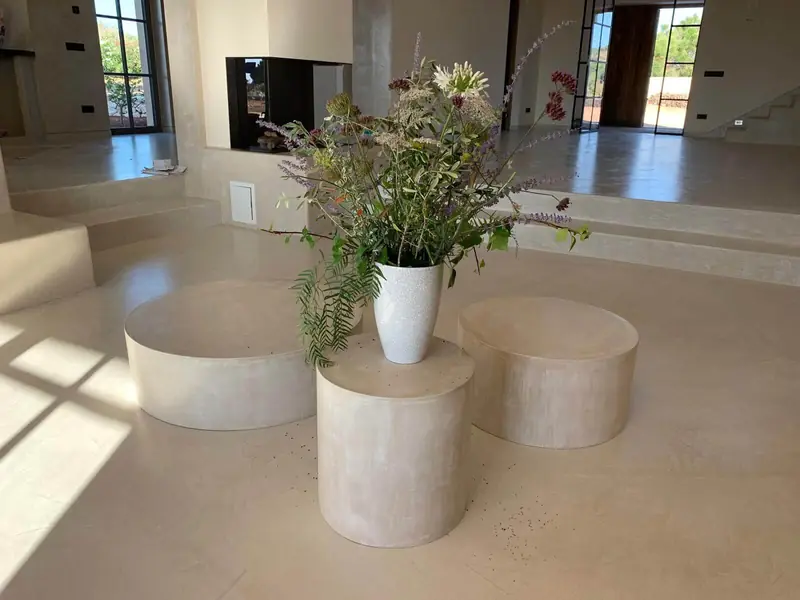 Mesas y pufs cilíndricos de microcemento en un salón luminoso