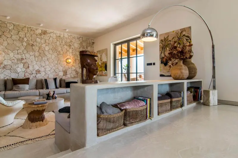 Salón con suelo de microcemento y estantería de obra revestida en microcemento, con pared de piedra al fondo