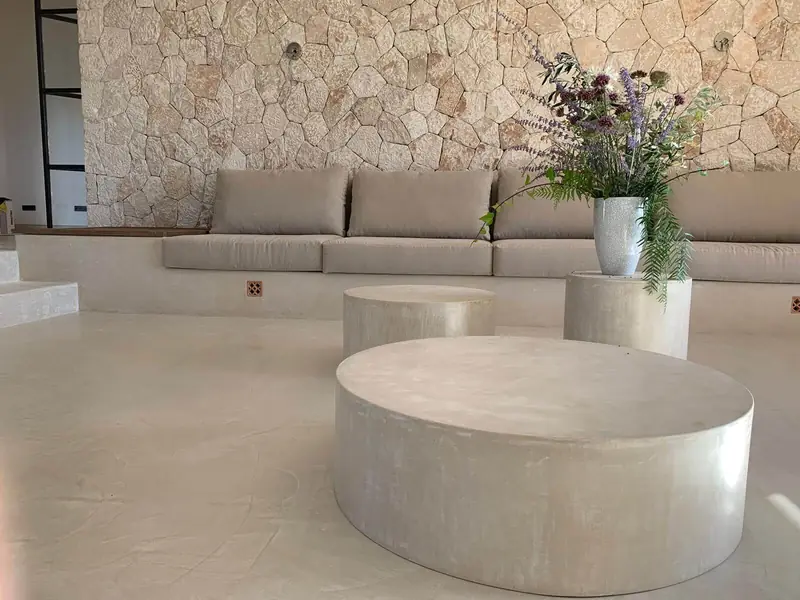 Sofá de obra y mesa redonda de microcemento ante una pared de piedra